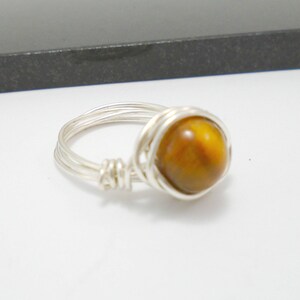 May include: A silver wire wrapped ring with a round, brown tiger's eye gemstone.