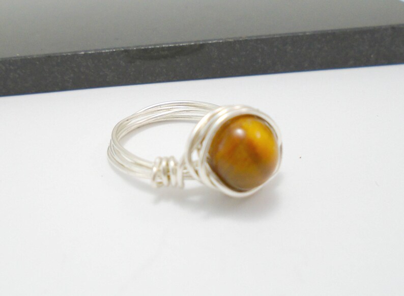 May include: A silver wire wrapped ring with a round, brown tiger's eye gemstone.