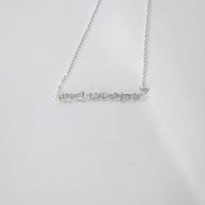 May include: A silver chain necklace with a bar pendant made of small, clear stones.