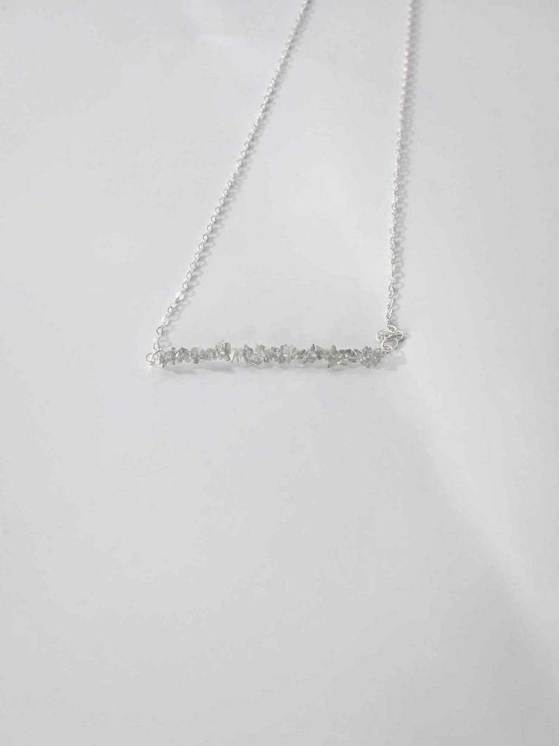 May include: A silver chain necklace with a bar pendant made of small, clear stones.