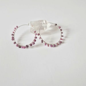 Op de afbeelding: Zilveren creolen met kleine roze edelsteen kralen die van de creolen hangen.