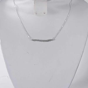 May include: A silver chain necklace with a thin, textured bar pendant.