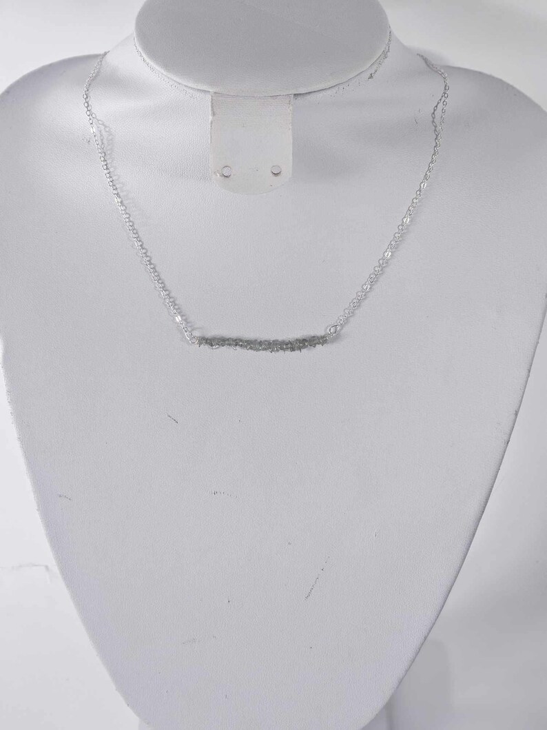 May include: A silver chain necklace with a thin, textured bar pendant.