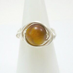 May include: A silver wire wrapped ring with a round, brown tiger's eye gemstone.