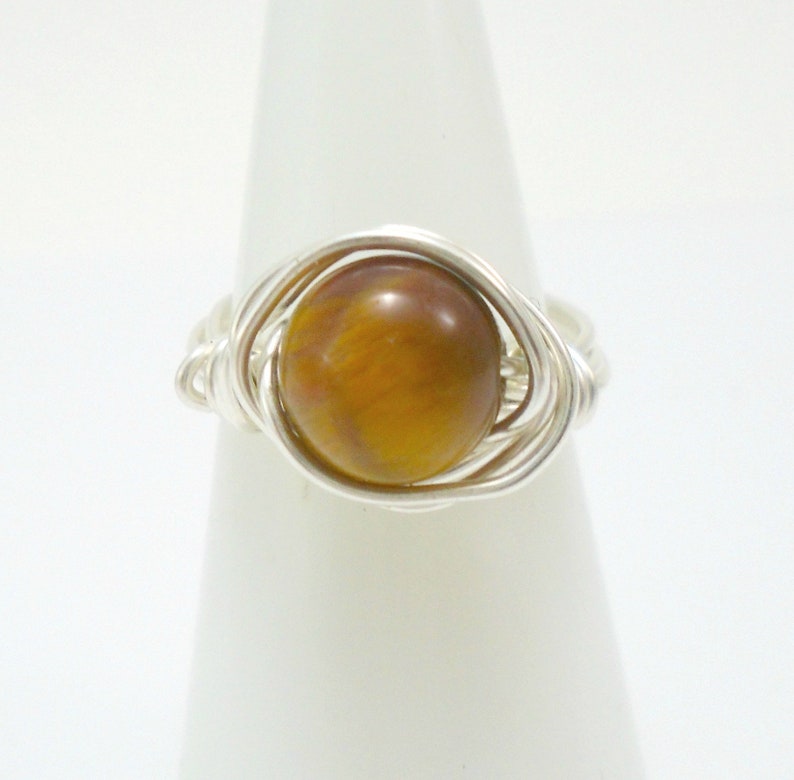 May include: A silver wire wrapped ring with a round, brown tiger's eye gemstone.
