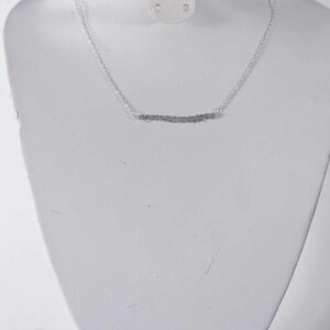 May include: A silver chain necklace with a delicate, wavy, silver bar pendant.