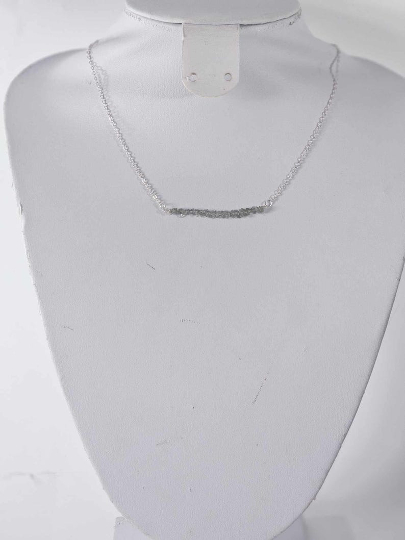 May include: A silver chain necklace with a delicate, wavy, silver bar pendant.