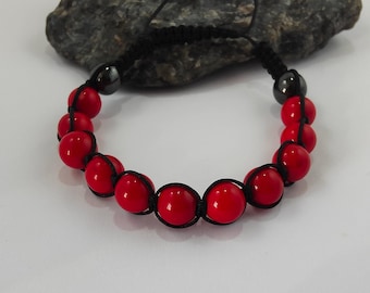 May include: Red beaded bracelet with black cord and adjustable closure. The bracelet features glossy red beads strung on a black cord, with black metal accents at the ends. The adjustable closure allows for a comfortable fit.