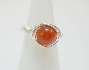 May include: A silver wire wrapped ring with a round, orange carnelian gemstone.