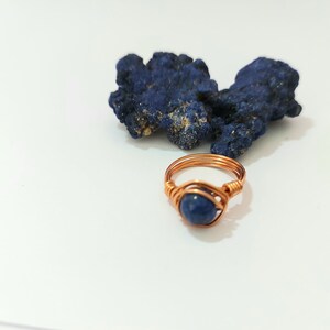 K&ouml;nnte beinhalten: Ein Ring aus Kupferdraht mit einem blauen Edelstein. Der Ring liegt auf einer wei&szlig;en Oberfl&auml;che neben einem St&uuml;ck blauen Azurite.