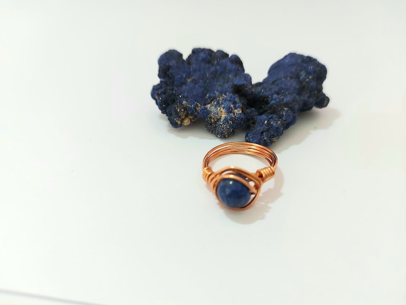 K&ouml;nnte beinhalten: Ein Ring aus Kupferdraht mit einem blauen Edelstein. Der Ring liegt auf einer wei&szlig;en Oberfl&auml;che neben einem St&uuml;ck blauen Azurite.