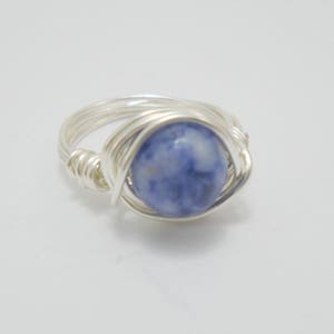 May include: A silver wire wrapped ring with a blue and white gemstone.