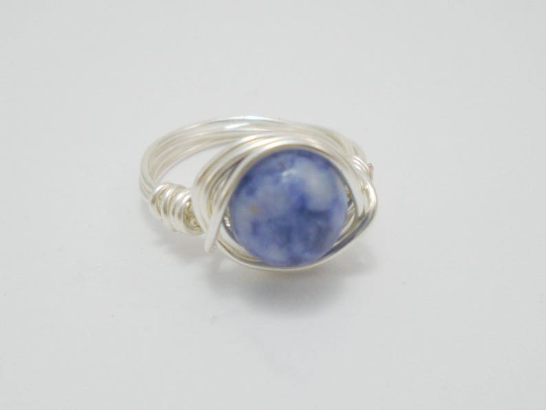May include: A silver wire wrapped ring with a blue and white gemstone.