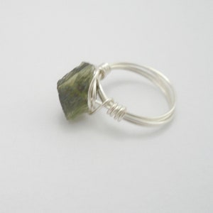 May include: A silver wire wrapped ring with a green gemstone. The gemstone is a rough, natural shape.