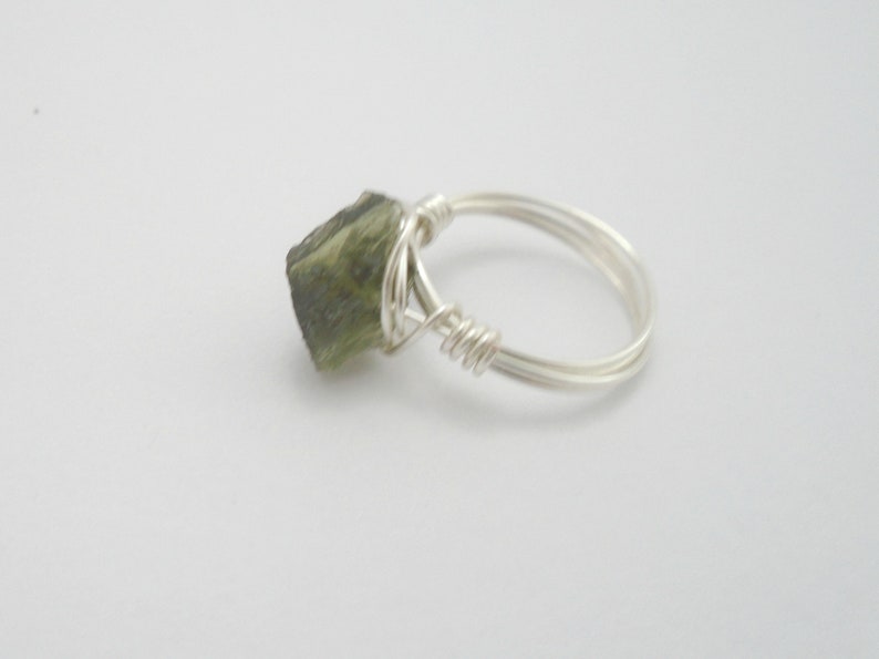 May include: A silver wire wrapped ring with a green gemstone. The gemstone is a rough, natural shape.
