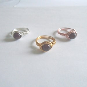 May include: Three wire-wrapped rings featuring black gemstone accents. The rings are crafted with silver, gold, and rose gold wire.