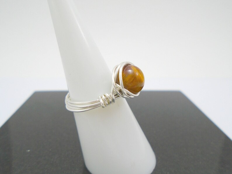 May include: A silver wire wrapped ring with a brown and gold tiger's eye stone.