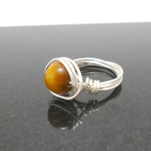 May include: A silver wire wrapped ring with a round, brown tiger's eye gemstone.