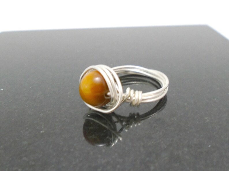 May include: A silver wire wrapped ring with a round, brown tiger's eye gemstone.