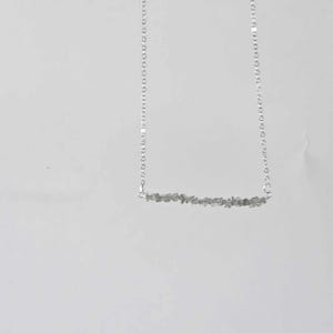 May include: A silver chain necklace with a bar pendant made of small, grey stones.