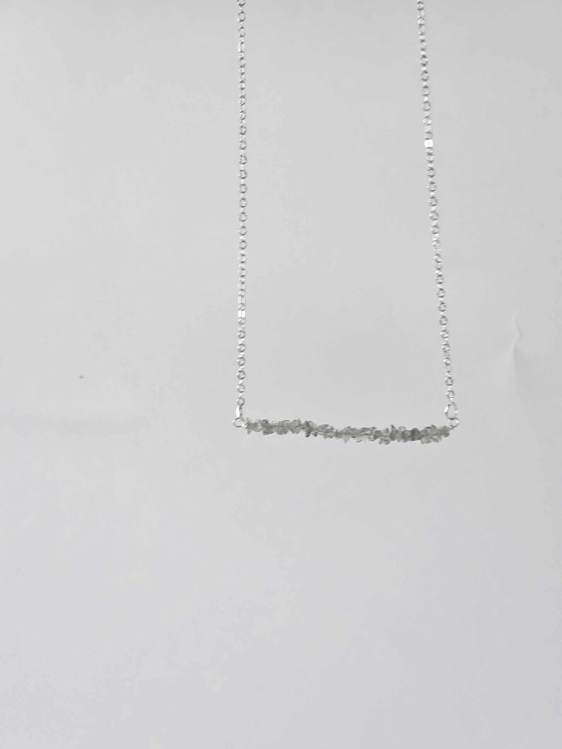 May include: A silver chain necklace with a bar pendant made of small, grey stones.