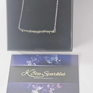 May include: A silver chain necklace with a bar pendant made of green gemstone chips. The necklace is displayed in a black box with a card that reads "K-Stie Sparkles - Bespoke Handmade Gifts".