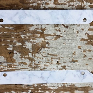 May include: White marble license plate frame with rounded corners and four holes for mounting.