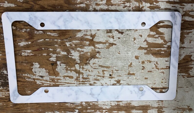 May include: White marble license plate frame with rounded corners and four holes for mounting.