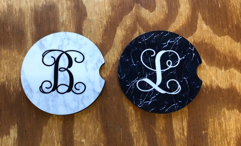 May include: Two round coasters with a marble design. One coaster is white with black marble veins and a black letter "B" with a swirl design. The other coaster is black with white marble veins and a white letter "L" with a swirl design.