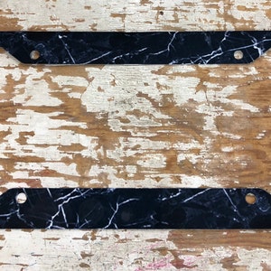 May include: Black and white marble license plate frame. The frame is made of plastic and has a smooth finish.