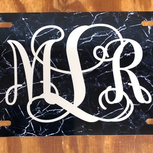 May include: Black and white marble patterned license plate with the monogram "MLR" in white.