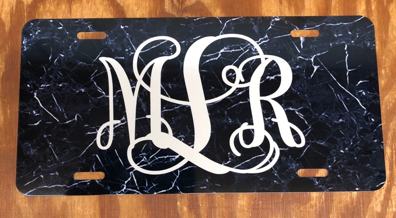 May include: Black and white marble patterned license plate with the monogram "MLR" in white.