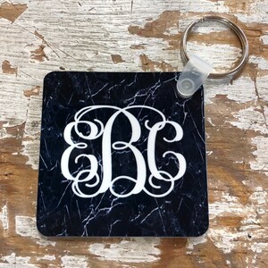 May include: A black and white marble-patterned square keychain with a white monogram "BC" in a script font. The keychain has a silver key ring attached.
