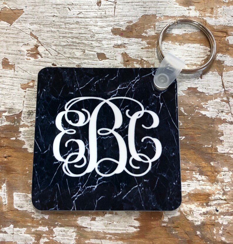 May include: A black and white marble-patterned square keychain with a white monogram "BC" in a script font. The keychain has a silver key ring attached.