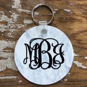 May include: White round keychain with a black marble pattern and a black monogram "MBS" in a script font. The keychain has a silver metal ring.