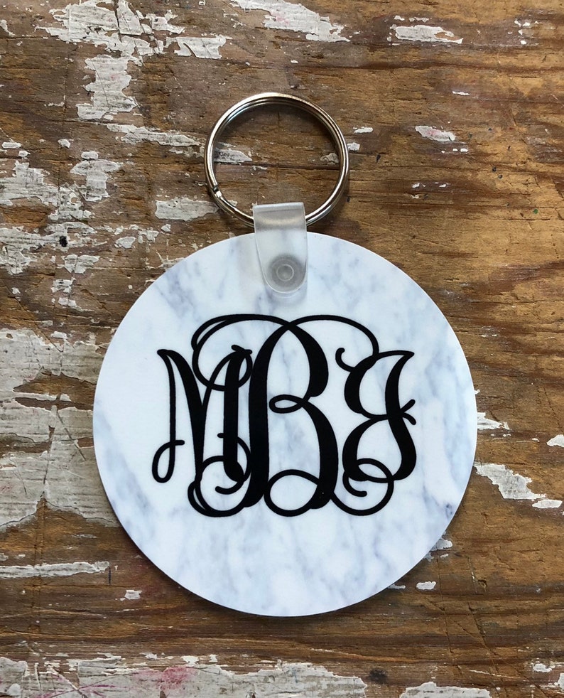 May include: White round keychain with a black marble pattern and a black monogram "MBS" in a script font. The keychain has a silver metal ring.
