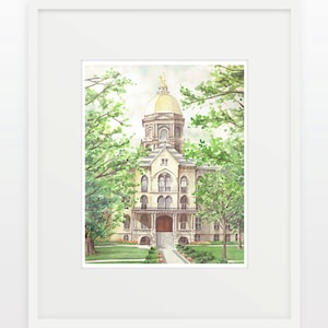 May include: Watercolor painting of a building with a gold dome, framed in white. The building is beige with arched windows and a portico. Lush green trees frame the building. The artwork is a framed print.