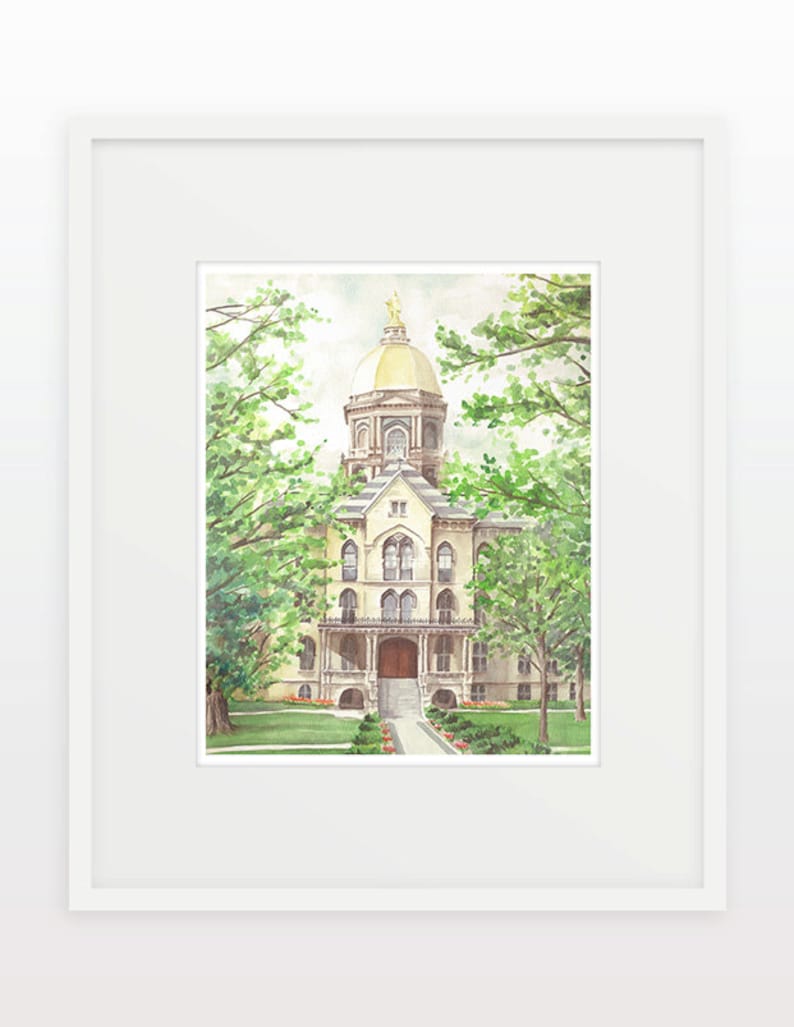 May include: Watercolor painting of a building with a gold dome, framed in white. The building is beige with arched windows and a portico. Lush green trees frame the building. The artwork is a framed print.