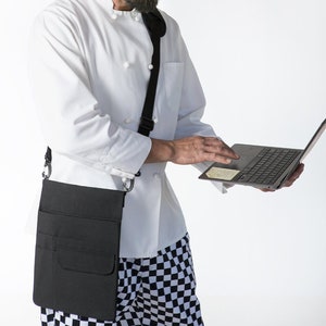 May include: A chef wearing a white chef's hat and a white chef's jacket with a black apron and black and white checkered pants is using a laptop computer.