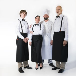 May include: Four people wearing black and white uniforms with black aprons. Two people are wearing bow ties. One person is wearing a chef's hat.