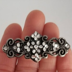 May include: A silver-toned hair clip with a floral design and white rhinestones.