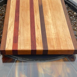 May include: A rectangular wooden cutting board with alternating vertical stripes of light and dark wood. The board features a natural wood grain pattern and is likely used for food preparation.