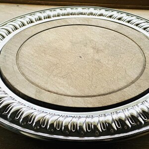 May include: A silver serving tray with a wooden insert. The tray has a decorative, scalloped edge.