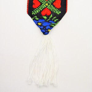 May include: A white tassel hangs from a black fabric with a colorful floral pattern. The pattern includes red, green, blue, and yellow.