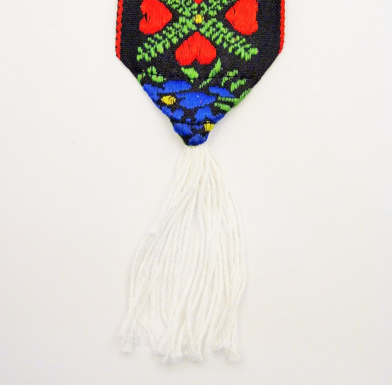 May include: A white tassel hangs from a black fabric with a colorful floral pattern. The pattern includes red, green, blue, and yellow.