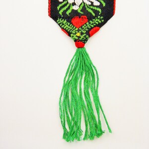 May include: A green tassel hangs from a black and red fabric bookmark with a white floral design.