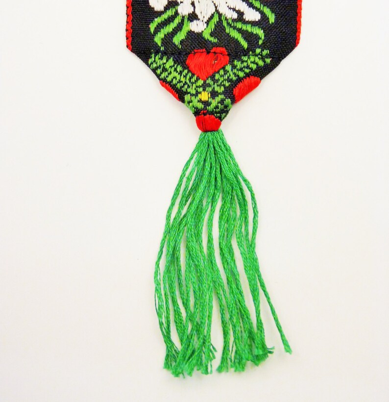 May include: A green tassel hangs from a black and red fabric bookmark with a white floral design.