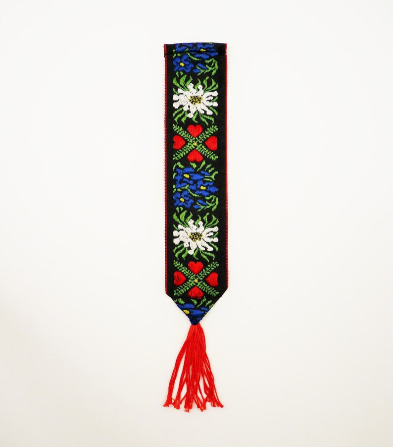 May include: A black bookmark with a red, white, and blue floral pattern and a red tassel.