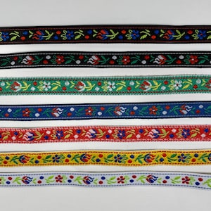 Könnte beinhalten: Sieben horizontal angeordnete Webbandstreifen, die jeweils ein wiederkehrendes Blumenmuster mit kleinen roten, blauen und weißen Blüten auf schwarzem, grünem, blauem, rotem, gelbem und weißem Hintergrund mit grünen Blättern zeigen.