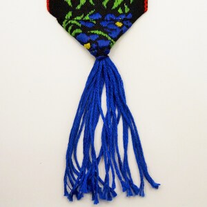 May include: A blue tassel hangs from a black and green fabric bookmark with a floral pattern.